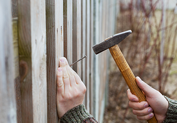 Someone using a hammer and nails to repair fence posts
